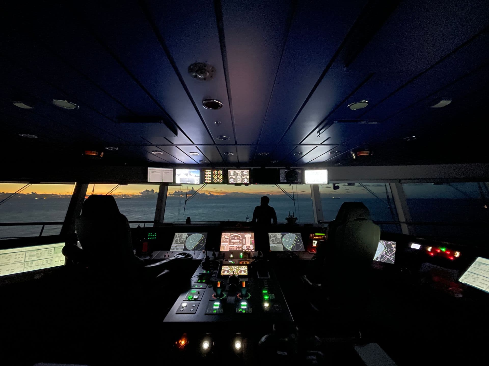 The bridge of a ship at dusk, an officer at the forward window keeping lookout